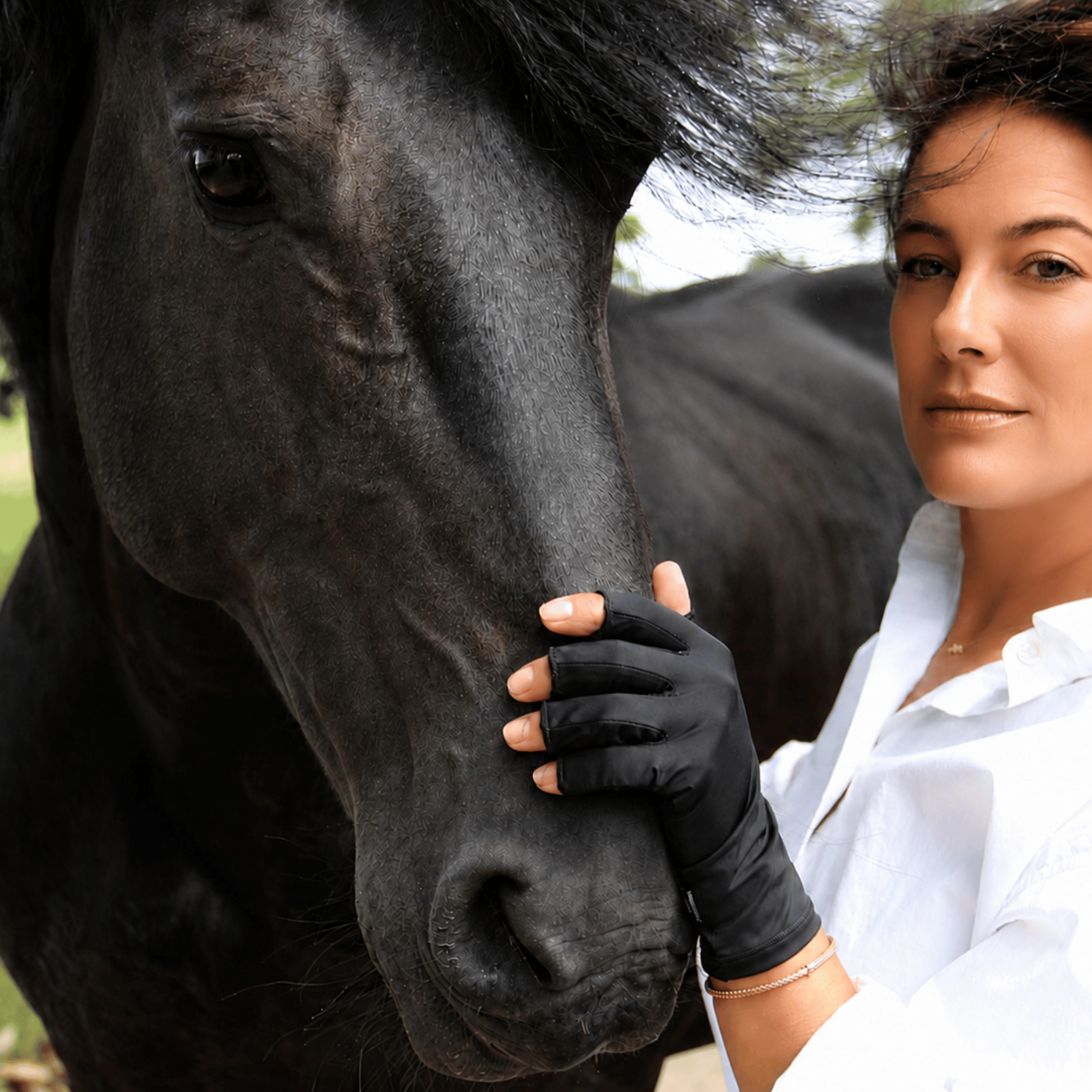 Vrouw met zwarte ONYX Handsome Skin UV-handschoen naast een zwart paard tijdens een buitenmoment.